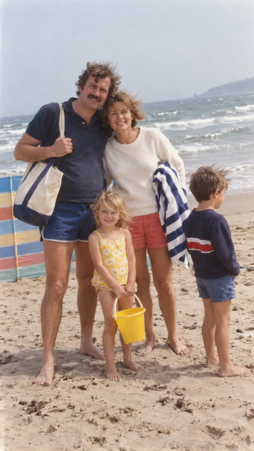 Family of four posing on a windy beach in a candid 1980s vacation snapshot