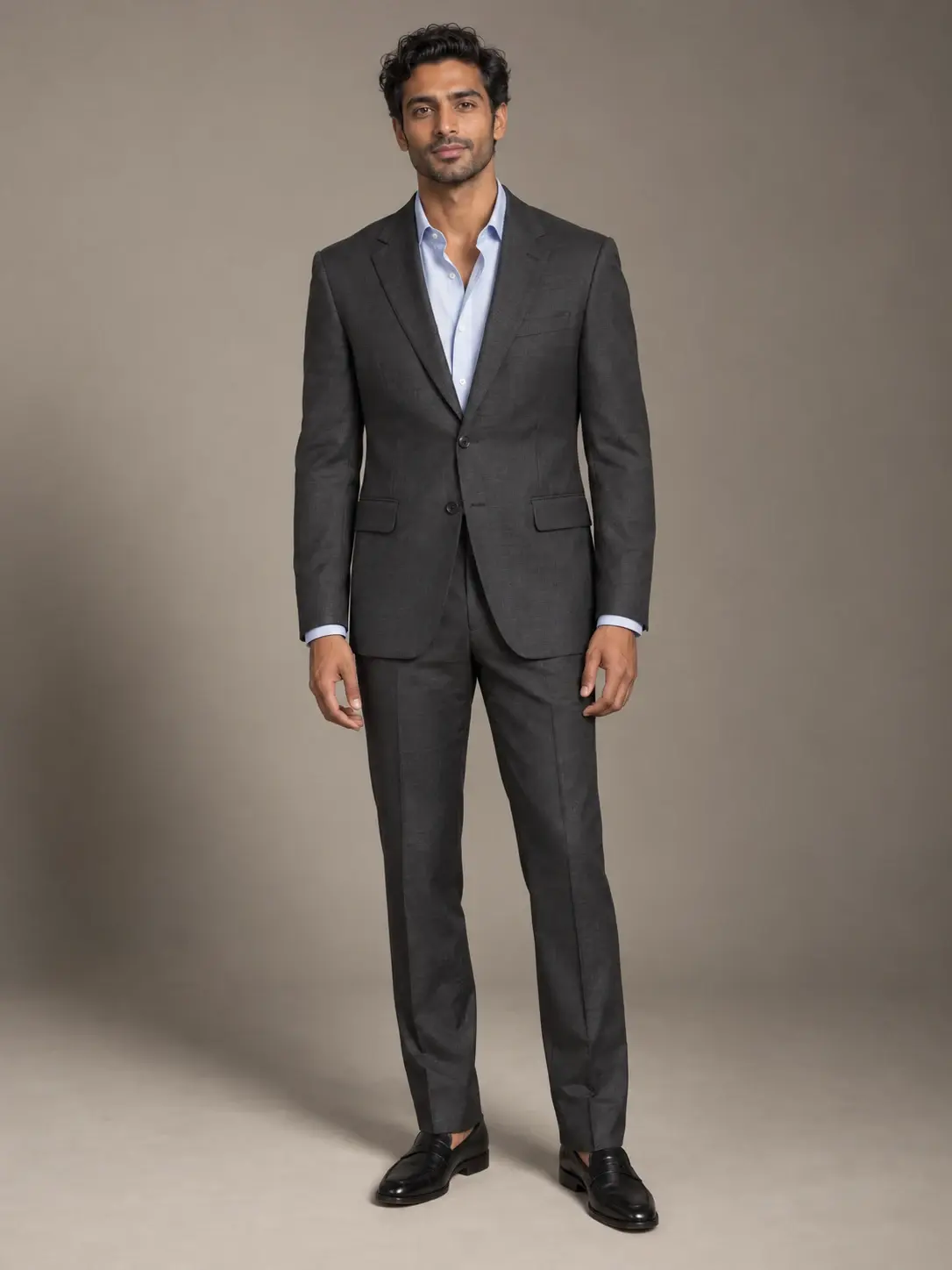 Adult wearing a charcoal suit and pale blue shirt against a warm gray studio backdrop.