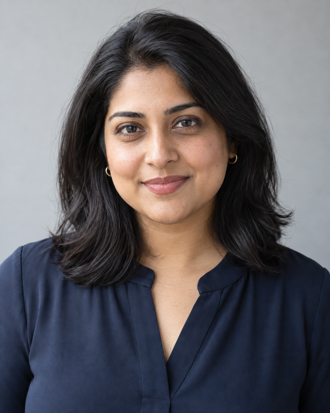 Woman in a navy blouse against a light-gray background with soft studio lighting.