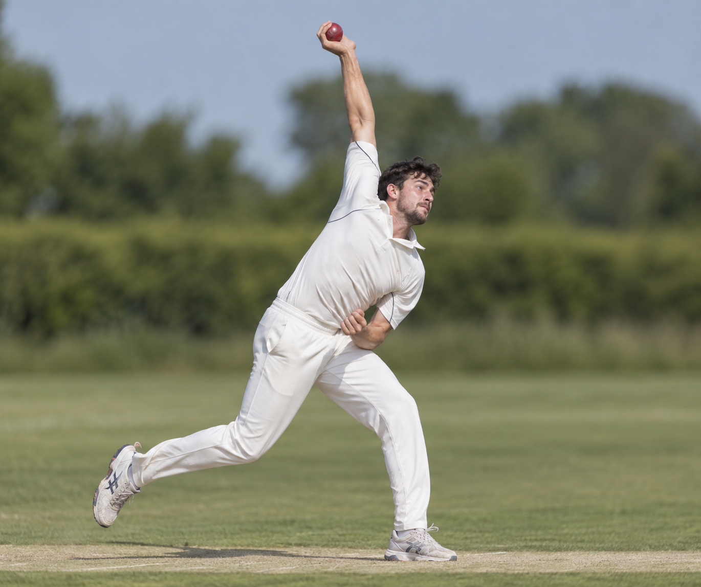 Cricket player in a pace-bowling delivery stride with the ball still overhead.