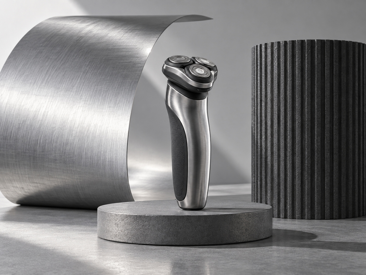 A silver electric shaver in front of brushed-metal and ribbed charcoal sculptures.