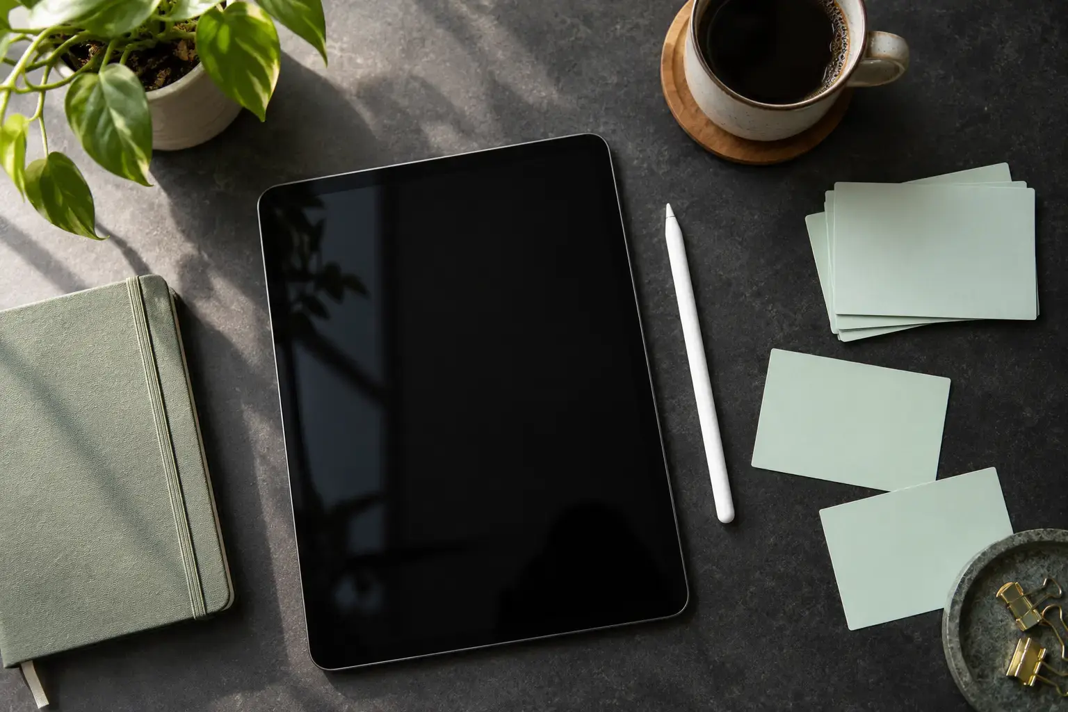 Overhead research planning workspace featuring a dark charcoal desktop with a screen-off tablet, mint task cards, a compact notebook and a stylus.